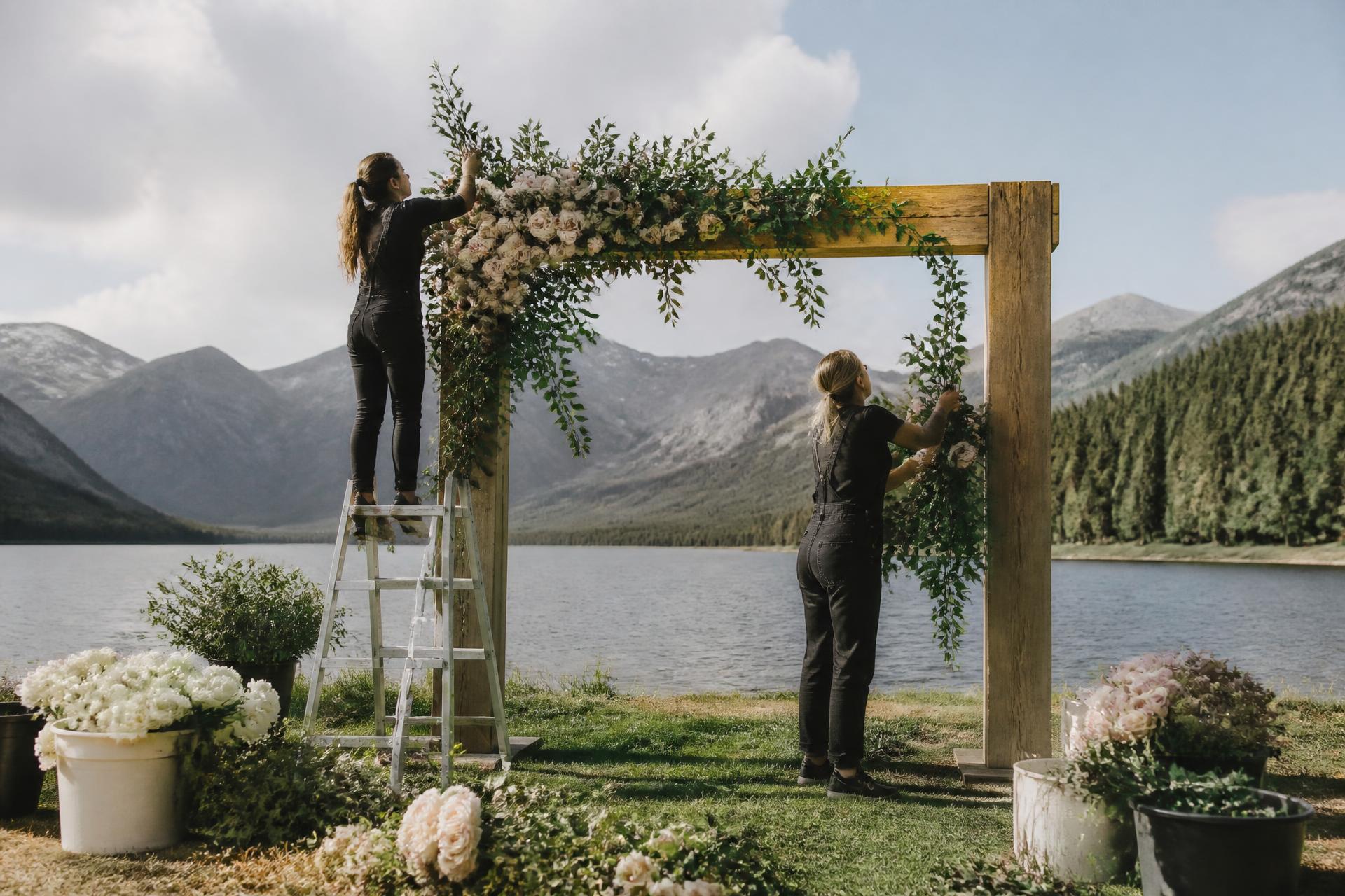 Florists installing blush and cream florals onto a lakeside ceremony arch