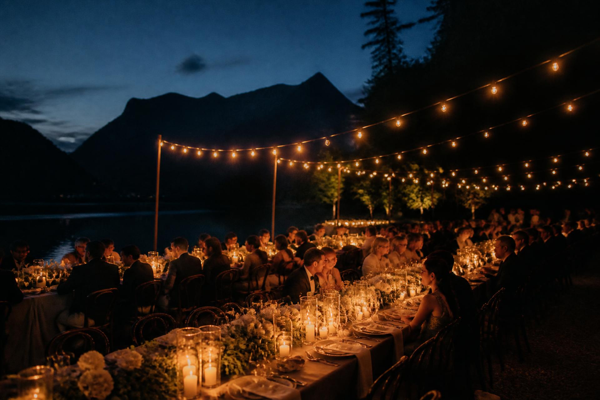 Candlelit evening reception with long tables beside a mountain lake